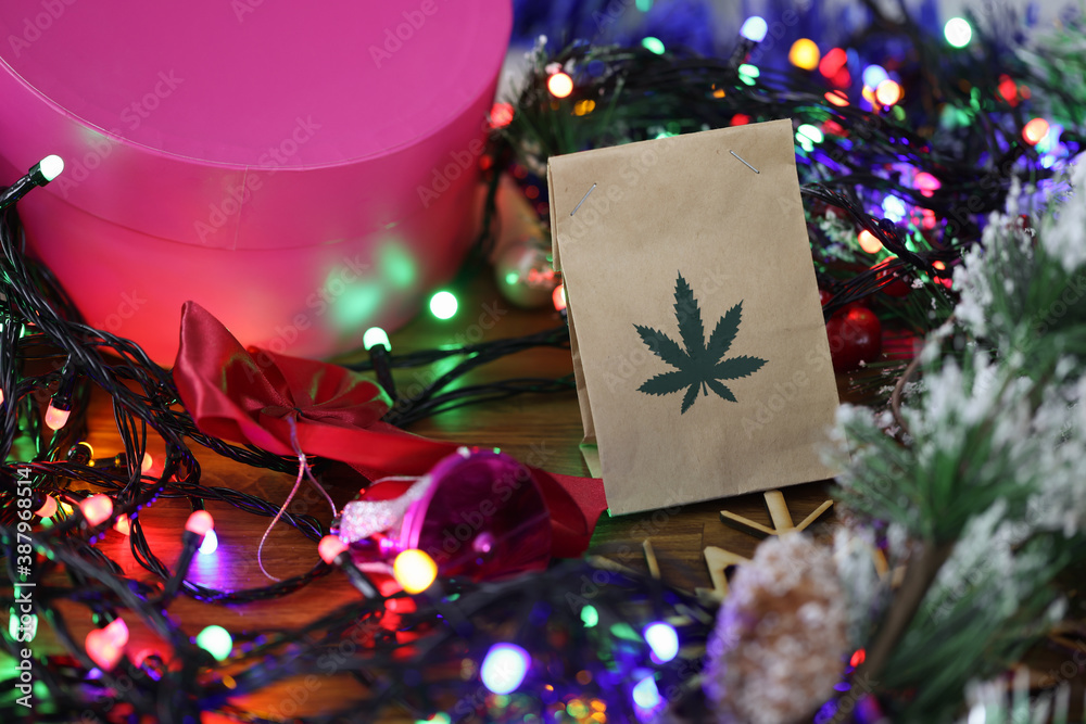 Wall mural paper bag with marijuana lies on table among new year's tinsel, gifts, garlands. legal sale of marij