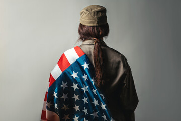 Celebration in the USA. A female soldier holds an American flag on a gray background on her shoulder. Copy space