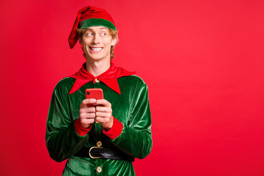 Photo of funky elf guy hold smartphone look copyspace wear green headwear isolated over red bright color background