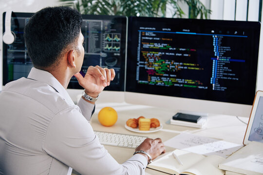 Pensive software developer working at his desk and checking mistakes in programming code on compter screen