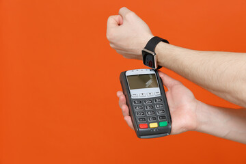 Cropped image of young man paying with smart watch wireless modern bank payment terminal to process acquire credit card payments isolated on bright orange colour background studio portrait.