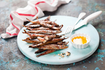 Fried capelin fish and butter sauce on a wooden plate, selective focus