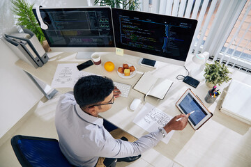 Software developer checking calendar on tablet computer when planning work on programming code for...
