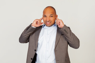 Portrait of unhappy young african american guy businessman, covering ears with fingers with annoyed facial expression trying not to hear bad singing and no pleasant sound Standing on a gray background