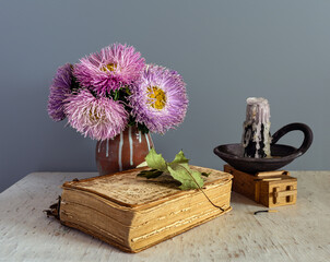Still life with a bouquet of asters, a book and an extinguished candle. Vintage.