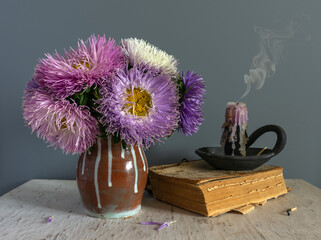 Still life with a bouquet of asters, a book and an extinguished candle. Vintage.