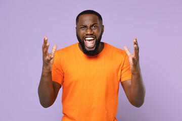 Fototapeta premium Angry irritated young african american man 20s wearing basic casual blank empty orange t-shirt standing spreading hands screaming swearing isolated on pastel violet colour background studio portrait.