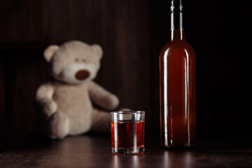 Child abuse concept. Teddy bear as a symbol of child's safety and bottle with glass on a wooden...