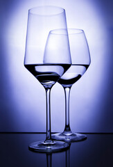 Two transparent glasses of wine with water on blue purple light background. Geometric and abstract concept