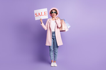 Full size photo of surprised nice girl hold purchases sale placard wear glasses coat jeans footwear isolated on purple background