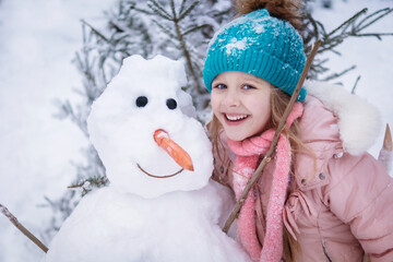 a little girl hugs a snowman with a carrot nose in winter