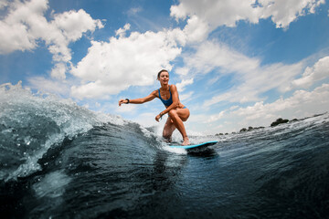 Athletic and active woman riding on wave sitting on surfboard against blue sky
