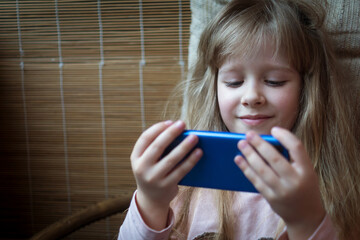 a little blonde girl is watching a video on her phone while sitting in a chair