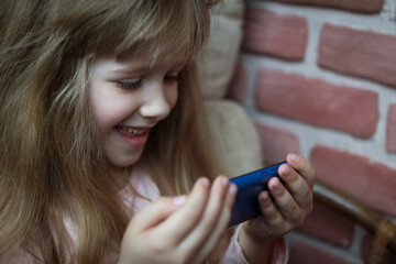 a little blonde girl is watching a video on her phone while sitting in a chair