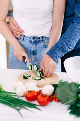 Husband hugs loving caring wife, chopping vegetables for salad on a cutting board.