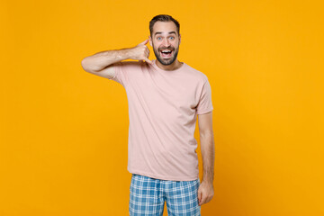 Excited young bearded man in pajamas home wear doing phone gesture like says call me back while resting at home isolated on yellow colour background studio portrait. Relax good mood lifestyle concept.