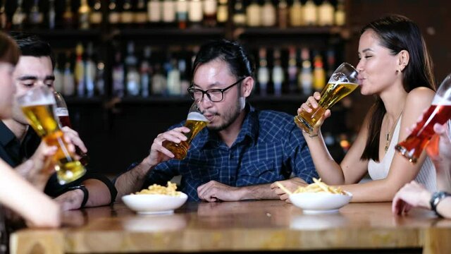 Happy young friends talking, having fun together drinking beer and clinking glasses in a fancy pub, celebrating xmas, new year or birthday party indoors, concept of friendship, holidays, celebration 