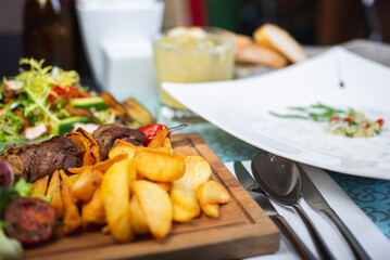 Meat, shish kebab, grilled, barbecue with baked potatoes and vegetables on a wooden plate on the table