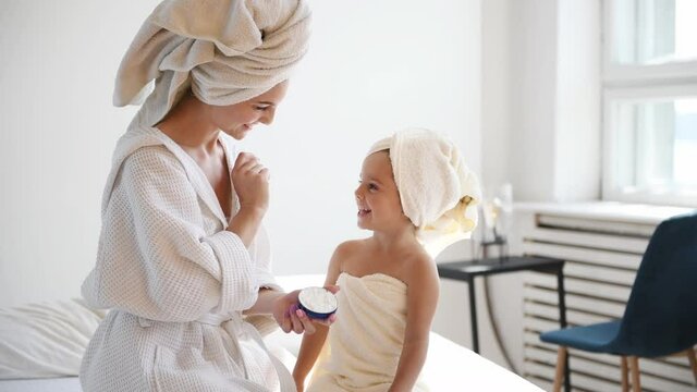 Young mother with her daughter putting cream on the skin.