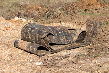 Heavily used destroyed cracked old rubber conveyor belt covered with dirt and sand left on side of construction site surrounded with rocks and dry grass on warm sunny winter day