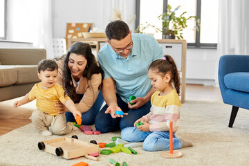 Fototapeta premium family and people concept - happy mother, father, little daughter and baby son playing with wooden toys at home