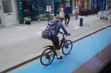 Schnelle Fahrradfahrerin auf Radweg in London mit Bewegungsunschärfe. Blauer Londoner Radweg auf der Straße neben dem Bürgersteig.