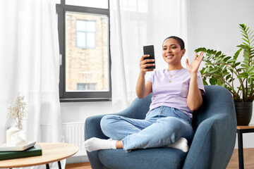 technology and people concept - smiling african american woman in glasses with smartphone having video call at home