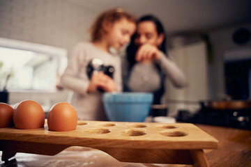 Closeup of brown eggs in tray with mother and child cooking in background in kitchen at home