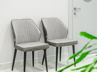 Two empty gray designer chairs, closed door with key and green houseplant in the foreground in a medical waiting room in a white clinic interior.