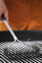 A man cleans the grate of a charcoal grill with a metal brush. Close up. Vertical image.