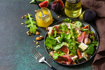 Healthy food concept. Autumn salad with figs, prosciutto, arugula, spinach, cheese, walnuts and honey on a stone countertop. Copy space.
