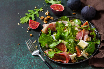 Healthy food concept. Autumn salad with figs, prosciutto, arugula, spinach, cheese, walnuts and honey on a stone countertop. Copy space.
