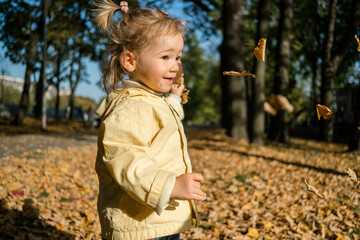 Caucasian child girl throws leaves in the park in autumn