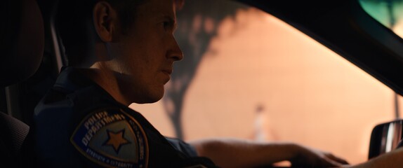 CU Portrait of police officer driving in a vehicle through city streets at night © supamotion