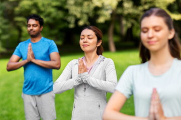 Obraz premium fitness, sport and healthy lifestyle concept - group of happy people doing yoga at summer park