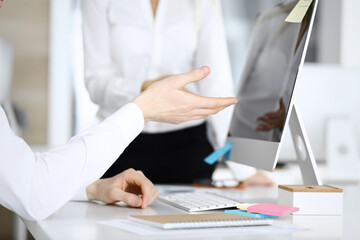 Businessman and woman are discussing questions while using computer and blocknote in modern office, close-up. Teamwork in business