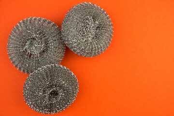 Top view of metal brushes for cleaning kitchen utensils on a bright orange background. Metal washcloths. Right Copyspace