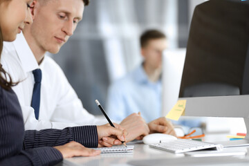 Business woman and man are discussing questions while using computer and blocknote in modern office, close-up. Teamwork in business