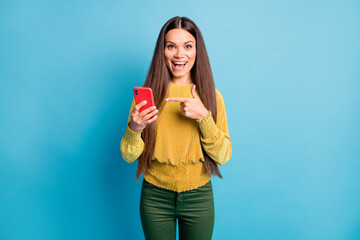 Obraz premium Photo portrait of woman holding phone in one hand pointing finger at it isolated on pastel blue colored background