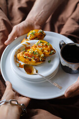 Serve Breakfast in bed. Male hands serve a plate of bruschetta and a Cup of coffee. A woman's hand with a silver bracelet takes the dish. The bed is made with plain brown linens.

