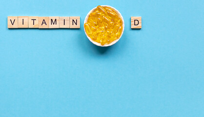 Yellow capsules in the round bowl and the word vitamin D from wooden cubes