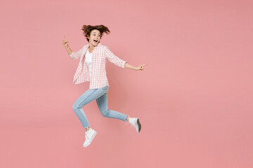 Fototapeta na wymiar Full length side view of excited funny shocked young brunette woman 20s wearing casual checkered shirt jumping pointing index finger aside isolated on pastel pink colour background, studio portrait.