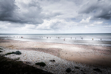 Manche sea, people out digging for razor clams at low tide in afternoon. On long sand beach with cloudy sky