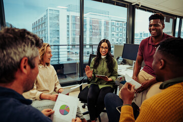 Indian designer raising hand to preset idea for new project smiling chatting to colleagues in office