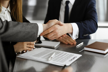 Unknown businessman shaking hands with his colleague or partner while standing straight in modern office, close-up. Business people group at meeting