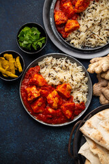 Chicken tikka masala dish with rice, flat Indian bread and spices in rustic metal plates on concrete background top view. Chicken tomato curry, turmeric root, fresh cilantro, traditional Indian meal