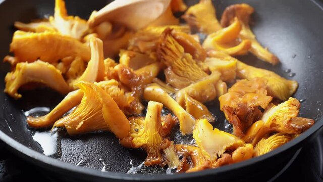 Close up of frying and stirring mashrooms chanterelles in a hot black pan with olive oil. Camera movement from left to right. Vegetarian healthy food. 4K UHD