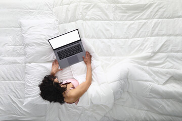 Woman lies on white bed with laptop. Remote work in quarantine in the coronavirus pandemic concept