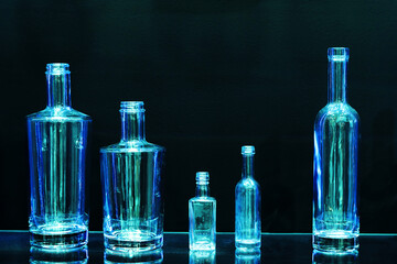 Glass bottles of various shapes on a dark background. Production of tableware for bottling alcohol