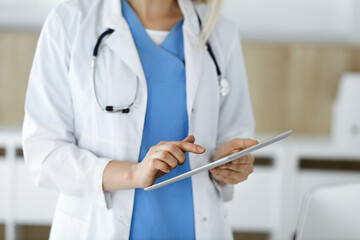 Unknown woman-doctor standing in clinic and using tablet pc, close-up. Data and best service in medicine and healthcare